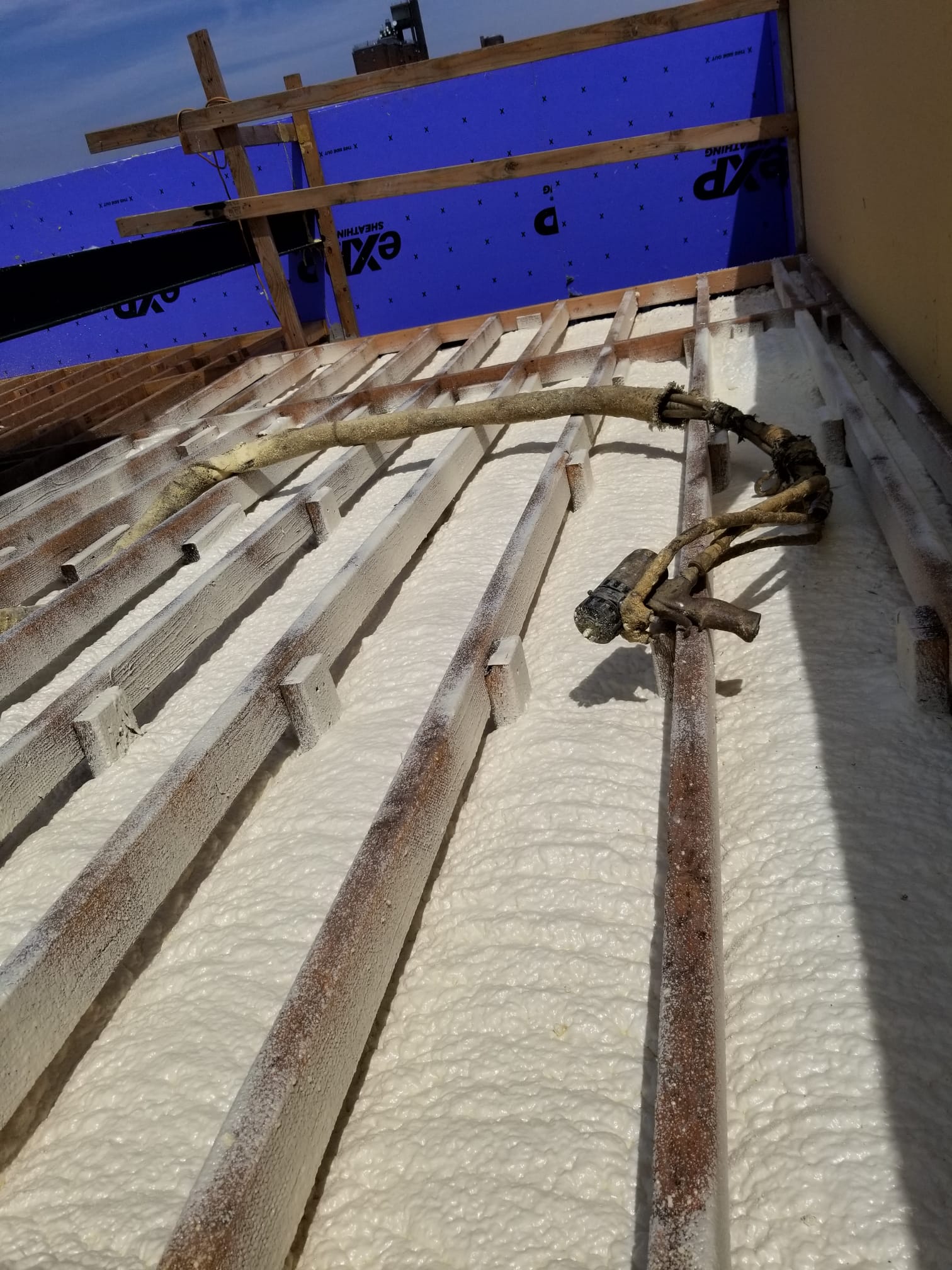 Foam sprayed between roof joists, spray gun resting on the frame